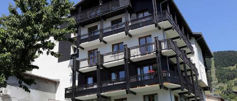 A multi-story building with balconies, stone facade, and parked cars.