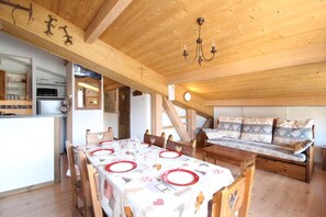 A cozy room with a wooden ceiling, a dining table set for four, and a sofa with patterned cushions.