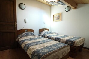 A room with two single beds, a wooden door, a ceiling fan, and a framed picture on the wall.