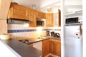 A compact kitchen with wooden cabinets, a microwave, a stove, and a refrigerator.