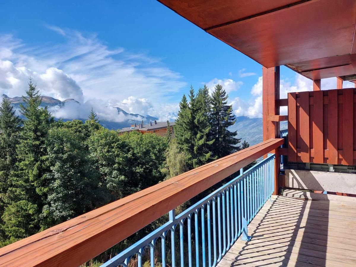 A wooden balcony with a blue railing overlooking a forested mountain area.