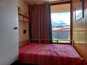 Un dormitorio con una cama, una estantería, una ventana con cortinas y vistas al exterior.