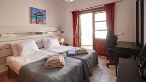 A hotel room with two beds, a desk, a chair, a TV, and a painting on the wall. - Casa Hannah - Marina Stroll by Villas Now (Playa Blanca)