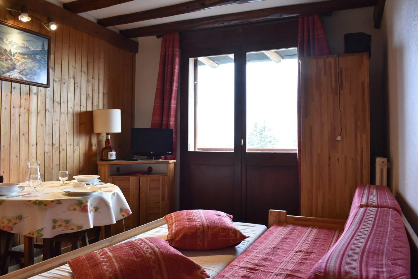 Une pièce chaleureuse avec un décor intérieur en bois, un lit avec une literie rouge, une petite table avec une lampe et un téléviseur.