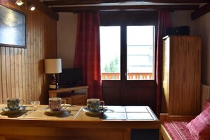 A wooden interior with a table set for two, a television, and a window with curtains. - 150m from ski slopes, 1st floor, balcony, tv, ski locker, 19m², Méribel (Méribel - Les Allues)