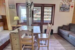 A compact living space with a wooden dining table, two chairs, a sofa, and a bed.