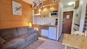 En kompakt opholdsstue med sofa, et lille tekøkken inklusive mikroovn samt et spisebord.