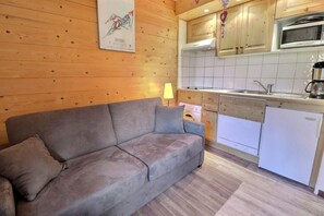 A cozy room with a sofa, a small kitchen area including a microwave, and a refrigerator.