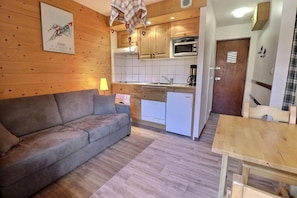 A compact living space with a sofa, a small kitchen area including a microwave, and a dining table.