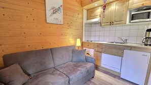 Et hyggeligt værelse med en sofa, et tekøkken med mikroovn og et køleskab.