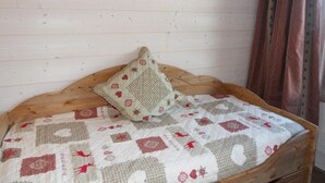 A bed with a quilted bedspread featuring geometric and floral patterns, a wooden headboard, and a single decorative pillow. - 50m from ski slopes, 4th floor, 18m², Méribel-Mottaret (Méribel - Les Allues)