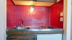 A compact kitchen with a red tiled backsplash, a stainless steel sink, and a built-in dishwasher. - 50m from ski slopes, 4th floor, 18m², Méribel-Mottaret (Méribel - Les Allues)