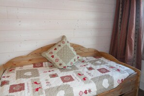 A bed with a quilt and a pillow against a wooden wall.