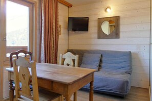 A wooden interior with a dining table, chairs, a sofa, a television, and a heart-shaped mirror. - 50m from ski slopes, 4th floor, 18m², Méribel-Mottaret (Méribel - Les Allues)