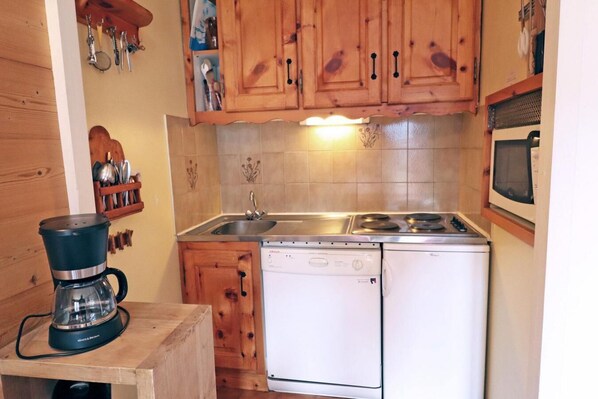Una cocina compacta con gabinetes de madera, un lavamanos, una estufa y un lavavajillas.