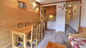 En inredning med trädetaljer, bestående av ett matbord och stolar, ett köksområde med träskåp och en liten sittgrupp med ett bord och kuddar.