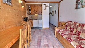 Ett mysigt rum med ett matbord och stolar i trä, en soffa med ett mönstrat överdrag och en köksdel med träskåp och diskmaskin.