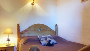 Un dormitorio con cabecera de madera, una mesita de noche con lámpara y una cama con almohada estampada.