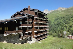 Tipico chalet plurifamiliare con balconi, sullo sfondo di montagne.