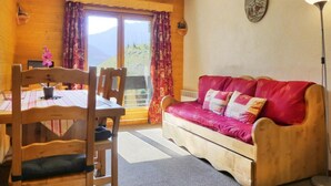 Una habitación acogedora con una mesa y sillas de madera, un sofá rojo y un amplio ventanal con cortinas.