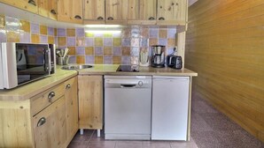 Cocina compacta con armarios de madera, microondas, cafetera y lavavajillas.