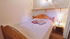 Ein kleines, gemütliches Schlafzimmer mit einem hölzernen Bett, einem Nachttisch mit Lampe und einer schlichten Wand.