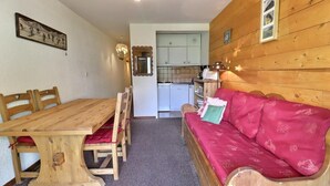 Ein gemütliches Zimmer mit einem Holzespeisetisch und Stühlen, einem roten Sofa, einer Küchenzeile und einem Spiegel an der Wand.