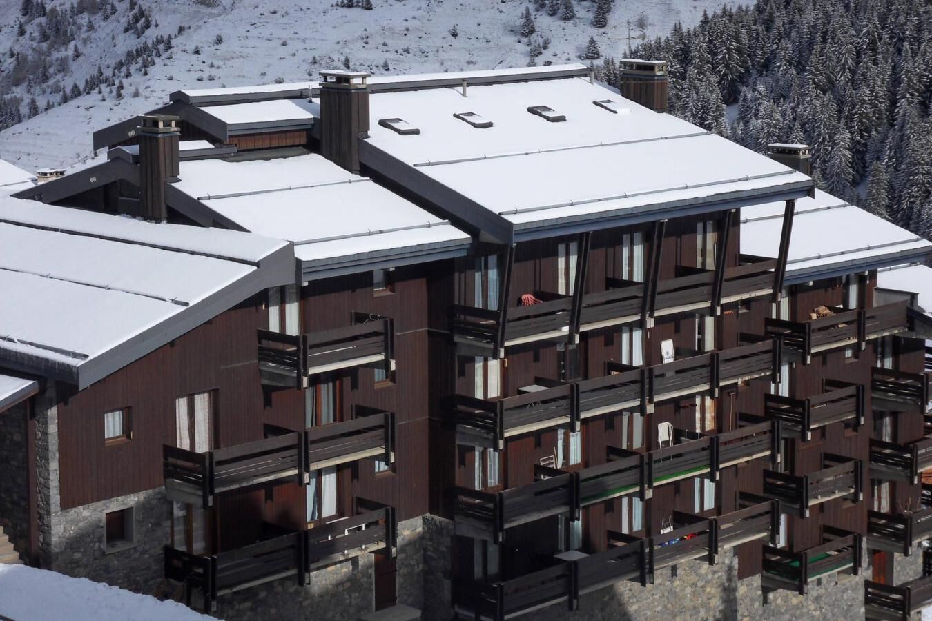 Um edifício moderno de vários andares com telhado coberto de neve, varandas e base de pedra.