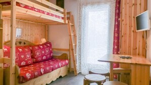 A wooden bunk bed with red patterned bedding, a small table with two stools, and a television on the wall. - 50m from ski slopes, Ground floor, 14m², Méribel-Mottaret (Méribel - Les Allues)