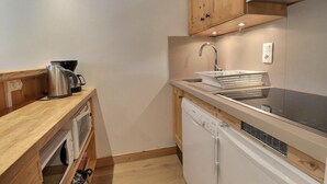 A compact kitchen with wooden cabinets, a built-in dishwasher, a kettle, and a sink with a drying rack. - 50m from ski slopes, 1st floor, balcony, fireplace or stove, 45m², Méribel-Mottaret (Méribel - Les Allues)