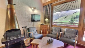 A cozy room with a fireplace, two sofas, a table, and a TV. - 10m from ski slopes, 3rd floor, balcony, fireplace or stove, 55m², Méribel-Mottaret (Méribel - Les Allues)