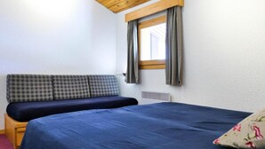 A bedroom with a bed, a bench with cushions, a window with curtains, and a radiator. - 10m from ski slopes, 3rd floor, balcony, fireplace or stove, 55m², Méribel-Mottaret (Méribel - Les Allues)