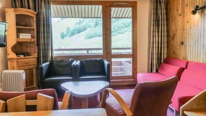 A cozy room with a wooden interior, a sofa, a red couch, a table, and a TV on a wooden cabinet. - 10m from ski slopes, 3rd floor, balcony, fireplace or stove, 55m², Méribel-Mottaret (Méribel - Les Allues)