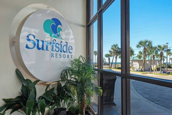 A sign for Surfside Resort with a view of palm trees and a building in the background.