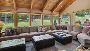 A spacious living room with a large sectional sofa, multiple ottomans, and a view of a green landscape through large windows. - A spectacular space for every season-in winter a real skier's destination! (Canaan Valley)