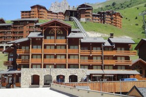 A multi-story lodge with wooden balconies, a ski lift, and a stone facade. - At the foot of shops, 1st floor, balcony, 22m², Méribel-Mottaret (Méribel - Les Allues)