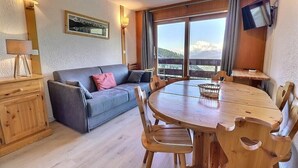 A cozy living room with a wooden dining table, a sofa, and a TV mounted on the wall. - 10m from ski slopes, 1st floor, balcony, 49m², Méribel-Mottaret (Méribel - Les Allues)