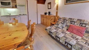 A cozy living area with a wooden dining table and chairs, a patterned sofa, a wooden cabinet, and a kitchen with a microwave and sink. - 10m from ski slopes, 1st floor, balcony, 49m², Méribel-Mottaret (Méribel - Les Allues)