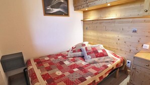 Quarto com cabeceira de madeira, colcha acolchoada e uma pequena mesa de cabeceira.