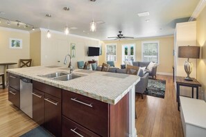 Une cuisine moderne dotée d’un grand îlot central, d’appareils électroménagers intégrés et de luminaires suspendus.