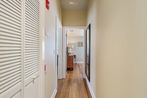 Un couloir étroit au plancher en bois, une porte dotée d’une poignée et un tableau encadré accroché au mur.