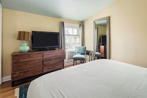 A hotel room with a bed, a television on a wooden dresser, a chair, and a window with curtains.