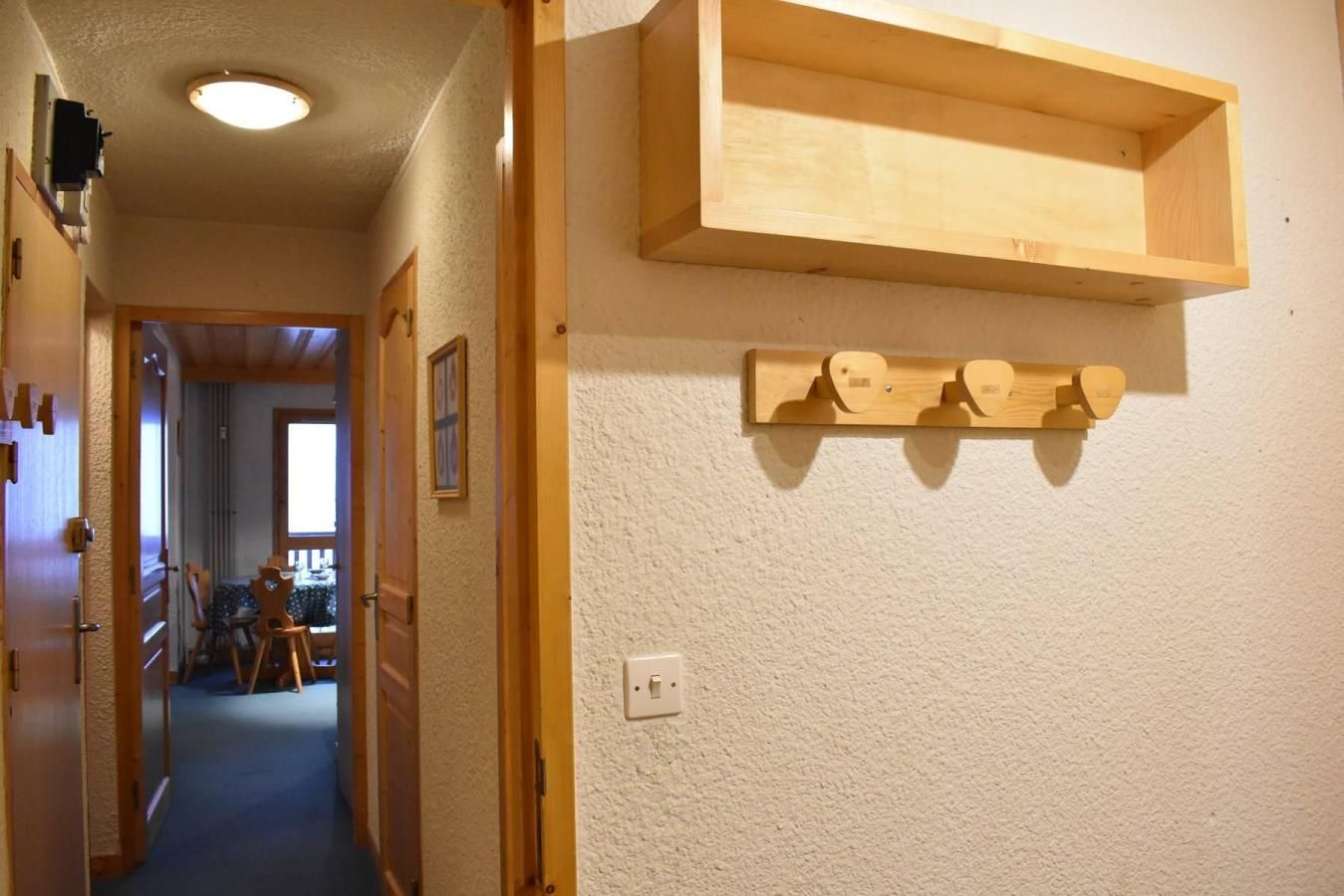 A hallway with a wooden shelf and wall-mounted hooks.