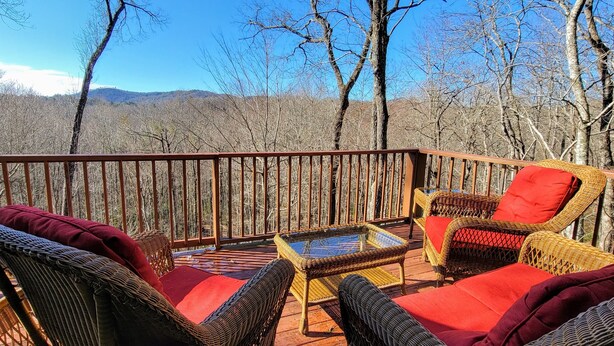 Eine Terrasse mit Korbmöbeln und roten Kissen, mit Blick auf eine bewaldete Landschaft und Berge in der Ferne.