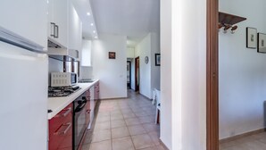 A modern kitchen with white cabinets, a red countertop, and a tiled floor.