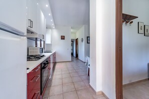 Cozinha moderna com armários brancos, bancada vermelha e piso ladrilhado.