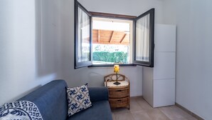 A small room with a blue sofa, a wicker side table with a lamp, and a window with open blinds.