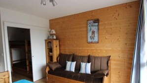 A cozy room with a brown sofa, a blue bedspread, and a wooden wall. - 10m from ski slopes, 1st floor, balcony, ski locker, 21m², Val Thorens (Val Thorens)