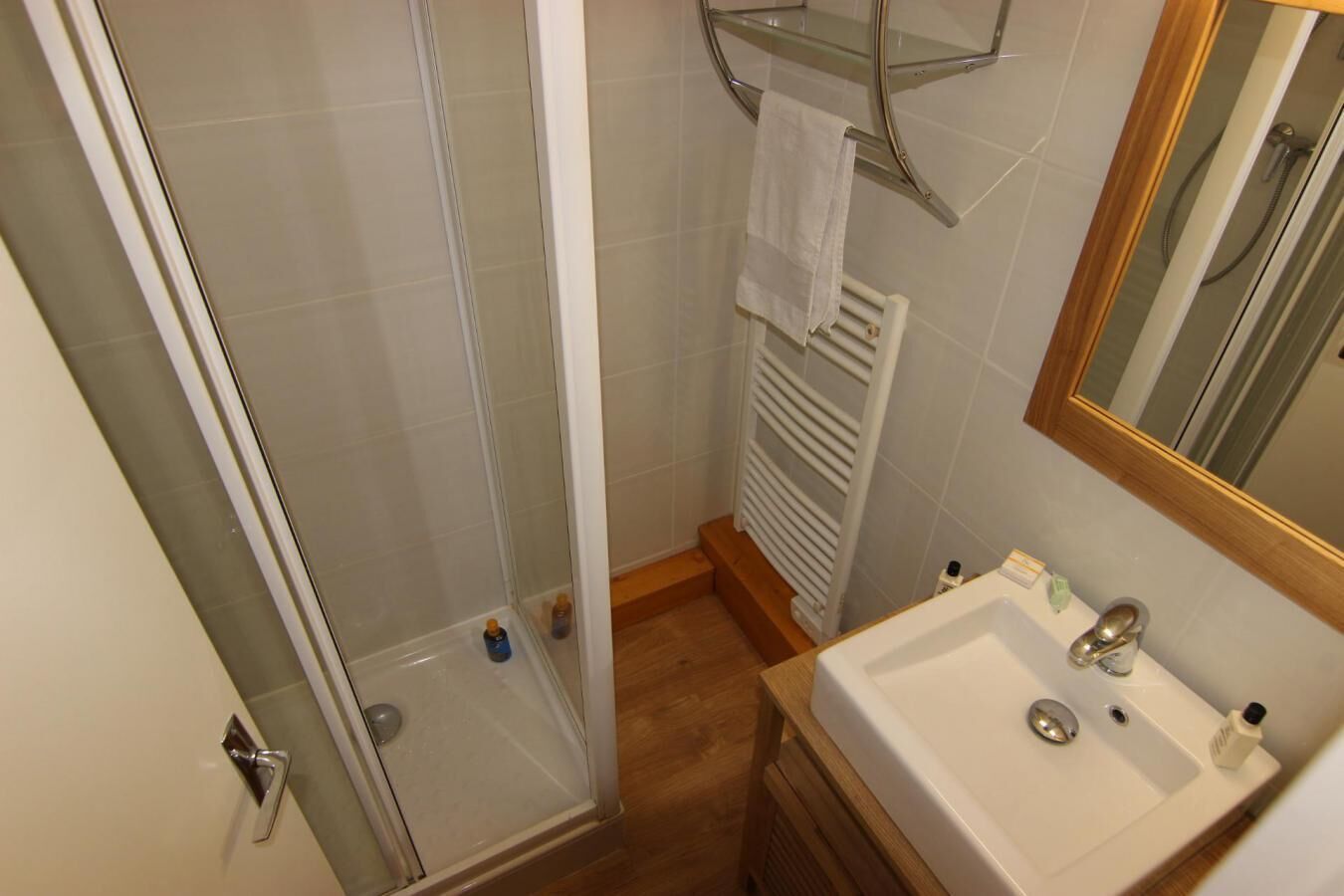 Un baño con cabina de ducha de vidrio, un lavamanos blanco con espejo y un perchero para toallas.