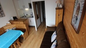 A cozy room with a wooden dining table, a brown sofa, and a kitchen area in the background. - 10m from ski slopes, 1st floor, balcony, ski locker, 21m², Val Thorens (Val Thorens)